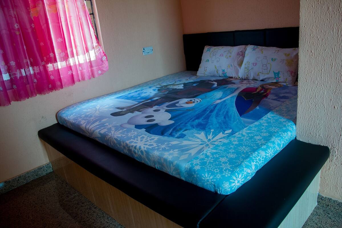 A bed with a blue and white snowflake pattern, a black headboard, and a pink curtain.