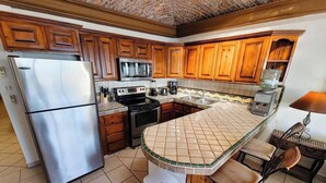 A kitchen with wooden cabinets, a stainless steel refrigerator, a microwave, a stove, and a tiled backsplash. - Family Condo Sea View Pool | 3bdr Sleeps 7 (Penasco)