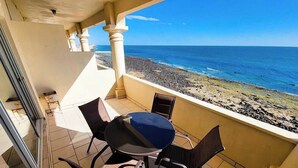 A balcony with a table and chairs, overlooking a rocky beach and the ocean. - Family Condo Sea View Pool | 3bdr Sleeps 7 (Penasco)