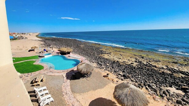 A beach resort with a swimming pool, lounge chairs, and a rocky shoreline. - Family Condo Sea View Pool | 3bdr Sleeps 7 (Penasco)