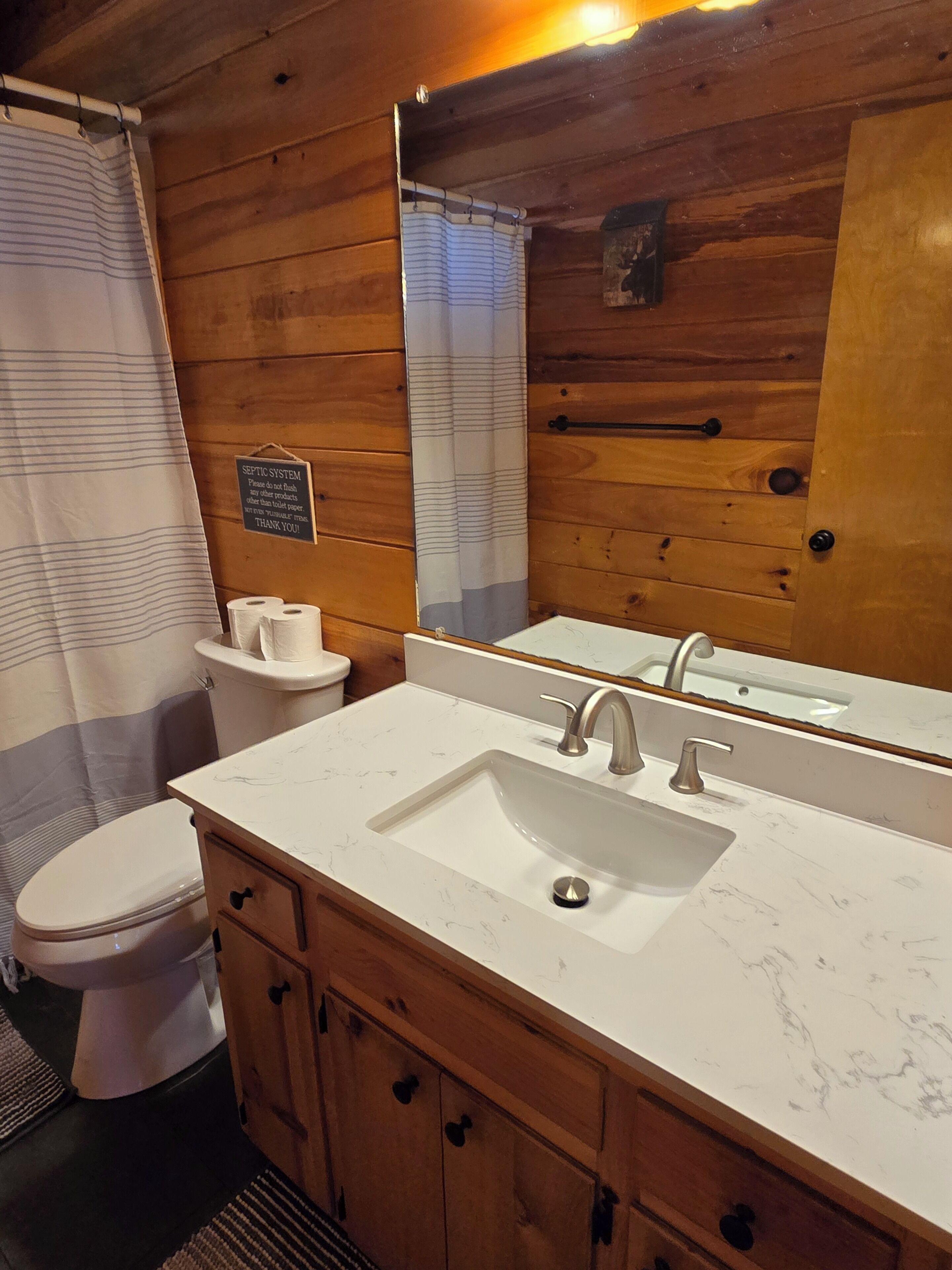 Une salle de bain rustique, avec des murs en bois, un lavabo blanc, des toilettes et un rideau de douche.