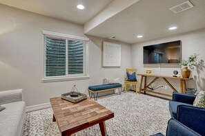 Ein gemütliches Wohnzimmer mit einem Holztisch, einem blauen Sofa, einem Holzstuhl und einem Fernseher an der Wand.