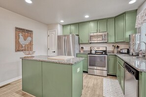 A kitchen with green cabinets, stainless steel appliances, and a granite countertop.