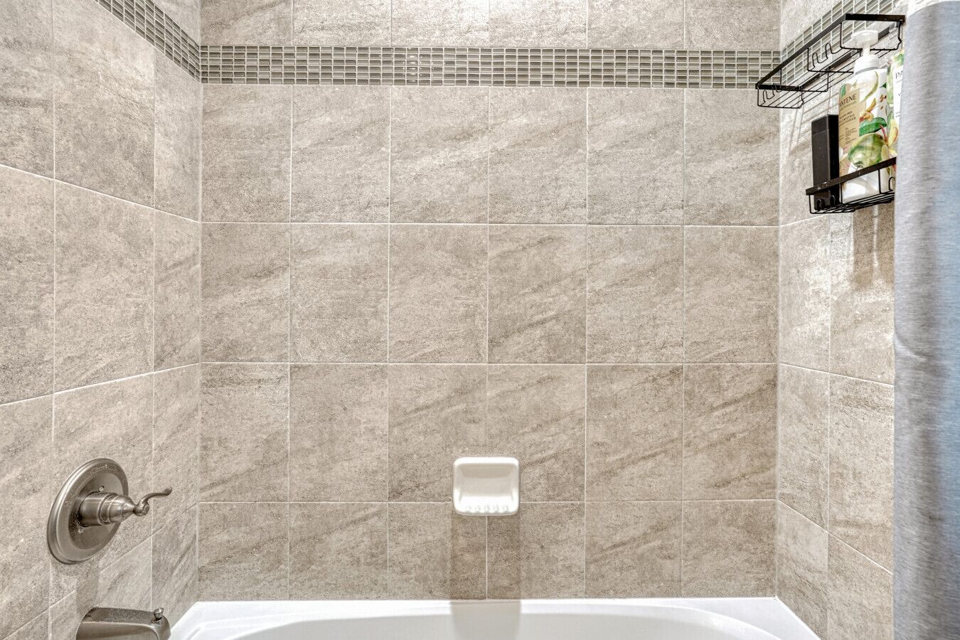 Un baño con bañera, zona de ducha y pared de azulejos.