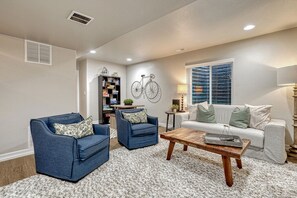 A living room with two blue armchairs, a wooden coffee table, a white sofa, and a bookshelf.