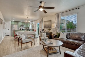 A spacious living room with a brown leather sofa, a round coffee table, and a dining area with a kitchen in the background.