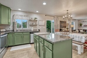 A modern kitchen with green cabinets, a granite countertop, and a dining area with a chandelier.