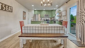 A dining area with a table set for two, a kitchen in the background, and a view of the outdoors through a large window. - Family Friendly Charming +Clean 5 Bedroom House, (Monument)