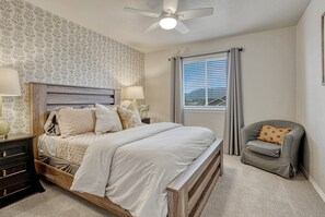 A bedroom with a bed, a nightstand, a chair, a window with curtains, and a ceiling fan.