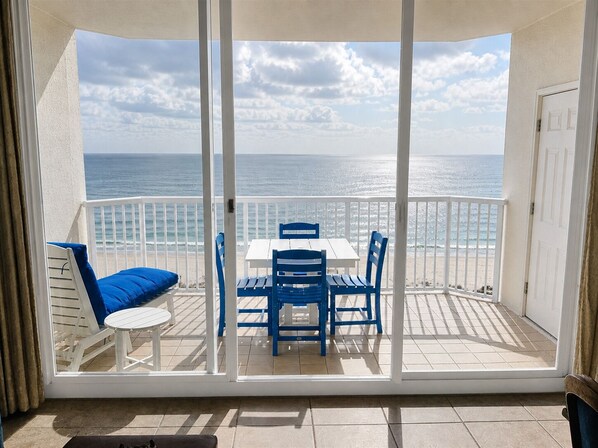 A balcony with a white table and blue chairs, overlooking the ocean.