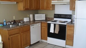 A kitchen with wooden cabinets, a white dishwasher, a stove, a microwave, and a refrigerator.