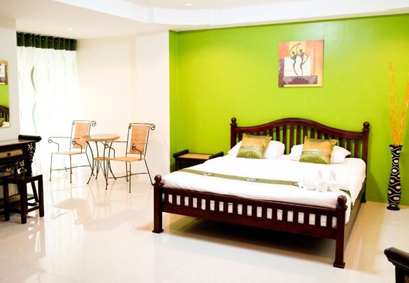 A bedroom with a wooden bed, green walls, and a painting. There is a small table and two chairs in the corner.