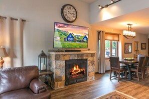 Una sala de estar con chimenea de piedra, un televisor montado encima y un comedor con sillas y una mesa.
