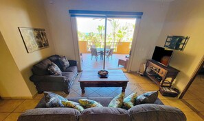 A living room with a sofa, a coffee table, a TV stand, and a balcony with outdoor furniture. - Bella Sirena B-202 2BR/2BA Upper Floor | Ocean Views & Luxury Sandy Beach Escape (Puerto Penasco)