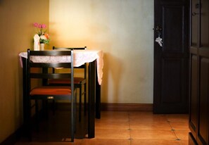 A dining area with a table set for two, a chair with a lace cover, and a vase with flowers.