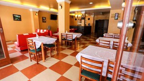 A restaurant with checkered flooring, red booths, and tables with lace tablecloths. - Sunshine Coast Inn (Pattaya)