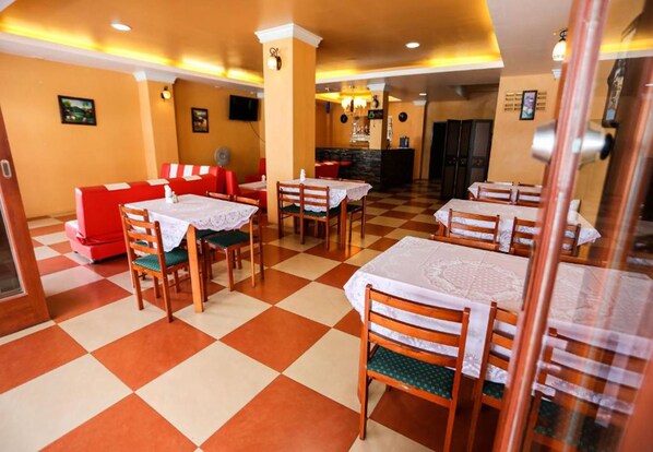 A restaurant with checkered flooring, red booths, and tables with lace tablecloths. - Sunshine Coast Inn (Pattaya)