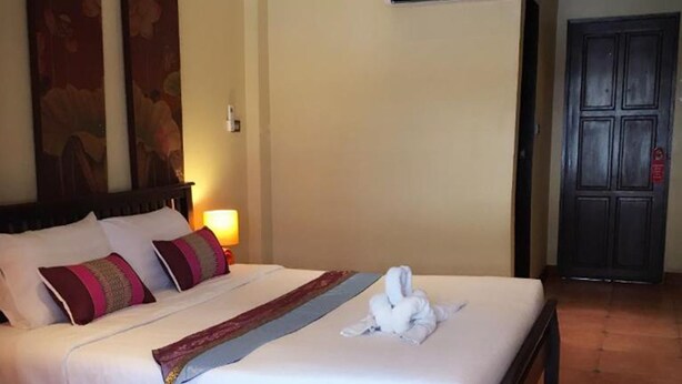 A hotel room with a large bed, a wall-mounted air conditioner, and a door with a security lock. - Sunshine Coast Inn (Pattaya)