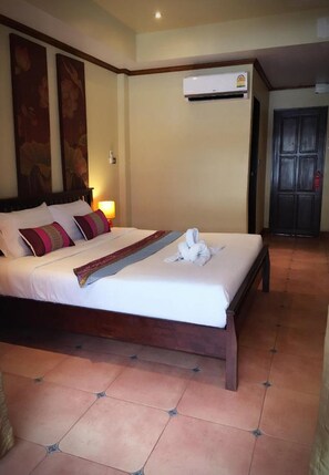 A hotel room with a large bed, a wall-mounted air conditioner, and a door with a security lock. - Sunshine Coast Inn (Pattaya)