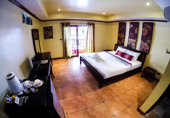 A hotel room with a bed, a desk with a computer, a chair, a coffee machine, and a table with a tray of items.