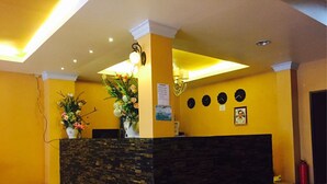 A reception area with a checkered floor, a reception desk with a vase of flowers, and a wall with clocks and a framed picture. - Sunshine Coast Inn (Pattaya)