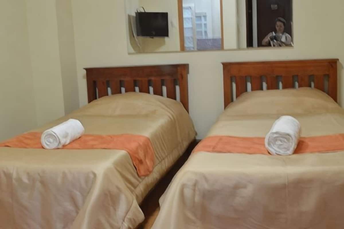 Two single beds with wooden headboards, orange bedspreads, and white towels.