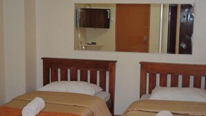 Une chambre avec deux lits, chacun doté d’une tête de lit en bois, d’un miroir au-dessus des lits et d’un téléviseur fixé au mur.