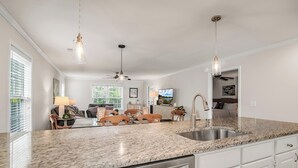 A kitchen with granite countertops, a dishwasher, and a sink. There is a dining area with a table and chairs, and a ceiling fan.