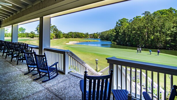 A covered outdoor seating area with chairs and a view of a golf course.