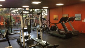 Un gimnasio con equipo de ejercicio, ventanas amplias y una pared roja.