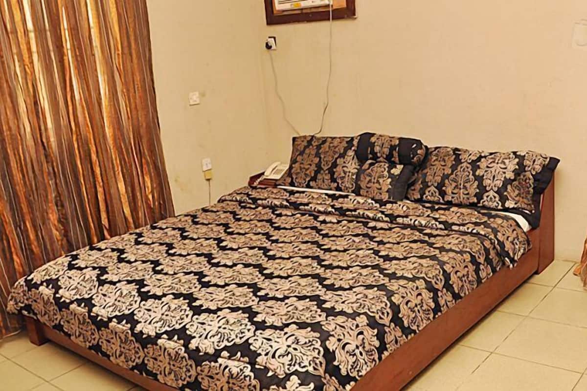 A bed with a patterned bedspread, a bedside telephone, and curtains on the walls.