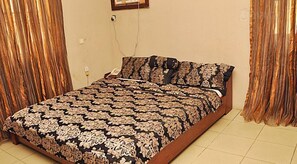 A bed with a patterned bedspread, a bedside telephone, and curtains on the walls. - Golden King Apartment Hotel (Lagos)