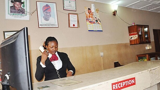 A reception desk with a 'RECEPTION' sign, a computer monitor, and framed certificates on the wall. - Golden King Apartment Hotel (Lagos)