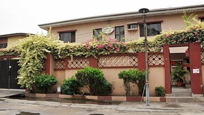 A building with a beige facade, decorative lattice panels, and a variety of potted plants and flowers. - Golden King Apartment Hotel (Lagos)