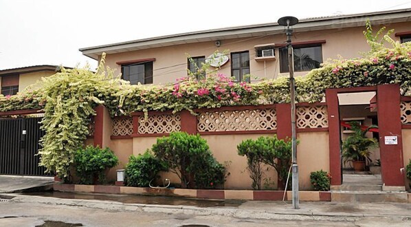 A building with a beige facade, decorative lattice panels, and a variety of potted plants and flowers. - Golden King Apartment Hotel (Lagos)