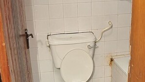 A bathroom with a toilet, a metal grab bar, and a damaged wall. - Golden King Apartment Hotel (Lagos)