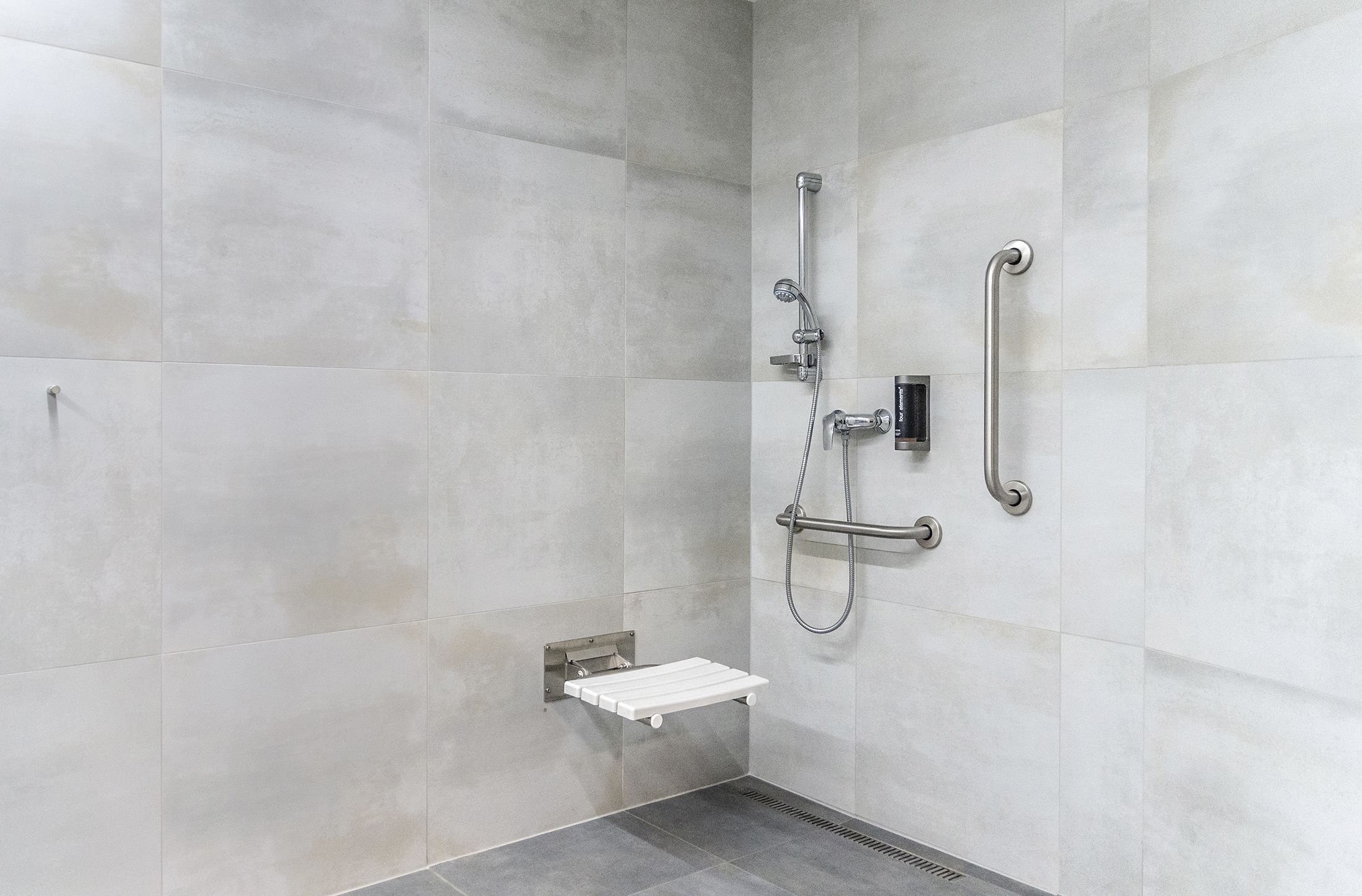 A modern shower area with a handheld showerhead, a wall-mounted faucet, and a grab bar for safety.