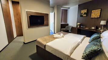Habitación de hotel con cama, escritorio, silla, televisor y obras de arte en la pared.