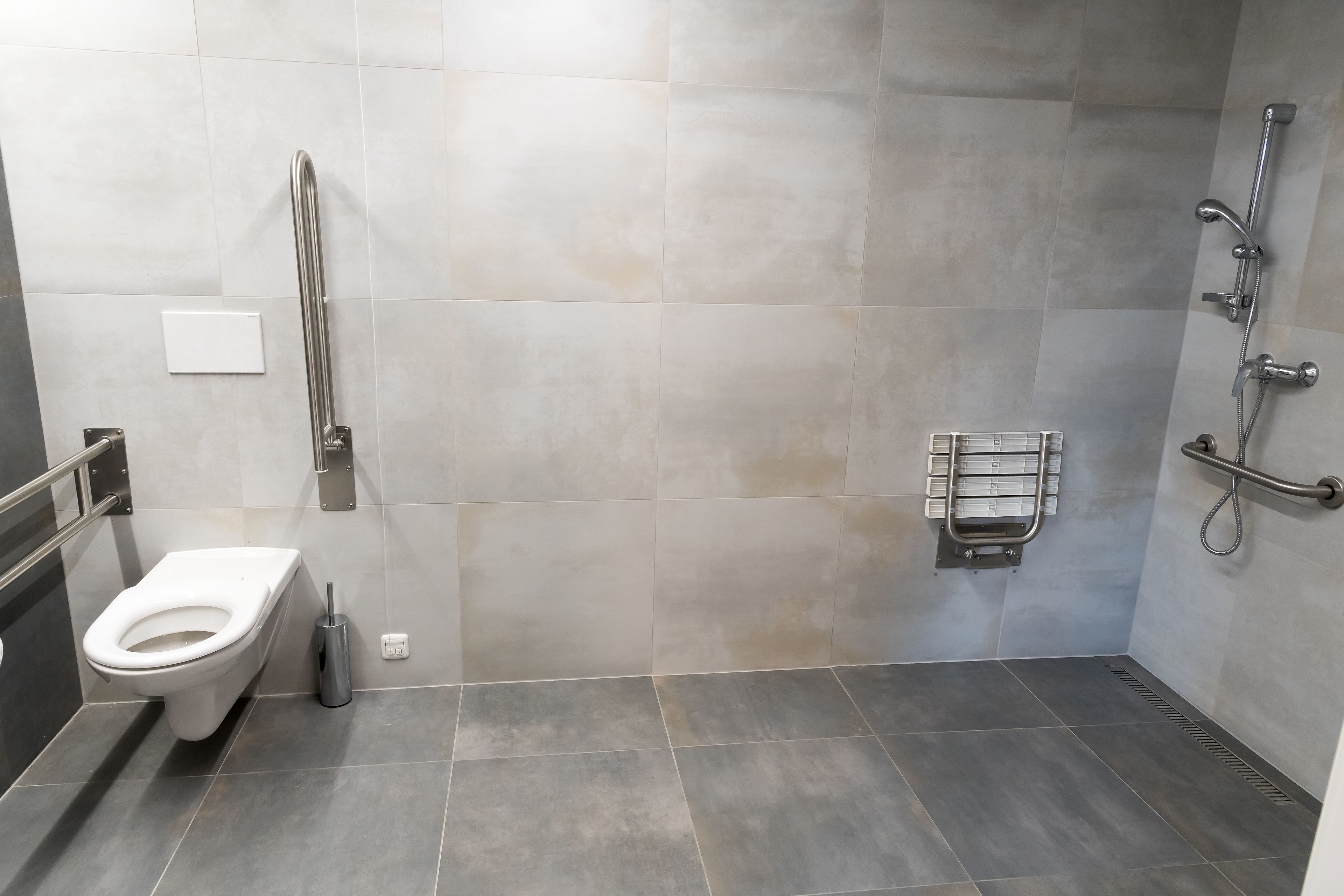 Une salle de bain moderne équipée de toilettes, d’une barre d’appui, d’un espace douche et d’un porte-serviettes.