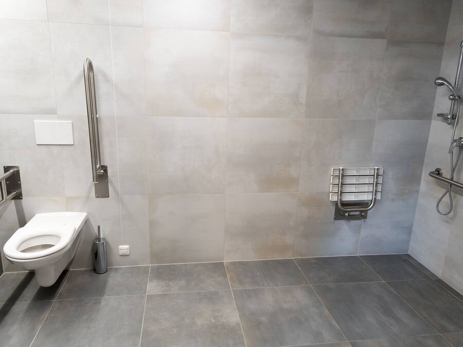 Une salle de bain moderne équipée de toilettes, d’une barre d’appui, d’un espace douche et d’un porte-serviettes.
