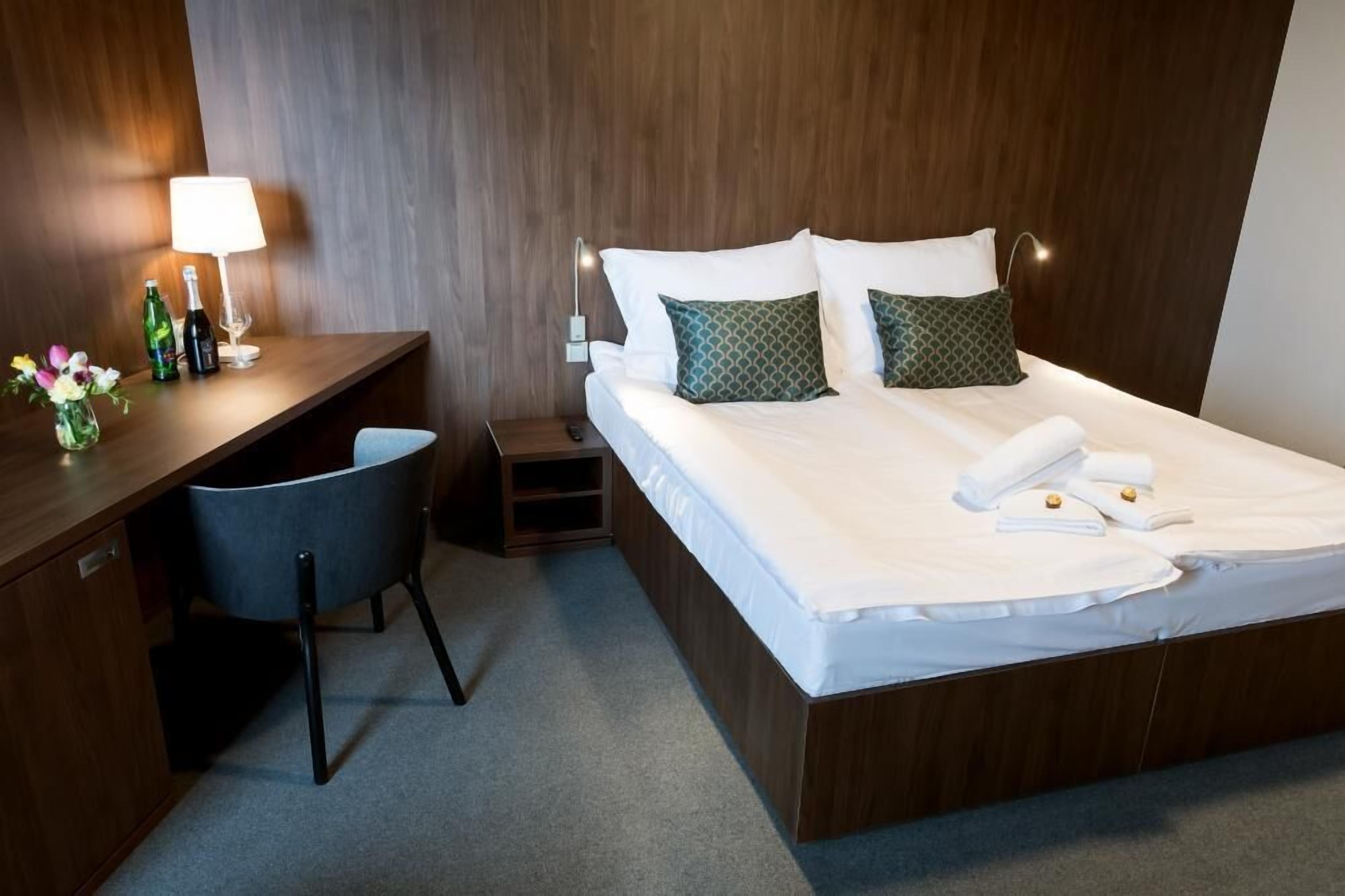 A hotel room with a wooden bed, a desk with a chair, a lamp, and a small nightstand.