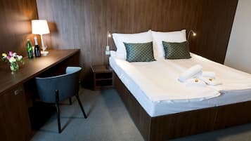 A hotel room with a wooden bed, a desk with a chair, a lamp, and a small nightstand.