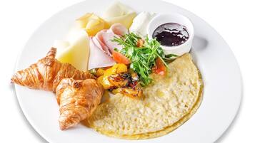 Um prato com um croissant, presunto, queijo, legumes e uma pequena tigela de geleia.