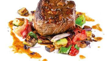 A steak with vegetables and sauce on a white plate.
