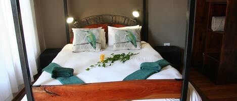Una cama con estructura de madera, ropa de cama blanca y dos almohadas con diseño de pájaros.