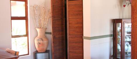 A room with a wooden door labeled "Toilet," a large vase with dried plants, a window, and a cabinet with glass doors.