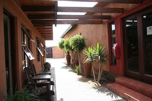 Un espace extérieur abrité, doté de bancs en bois, de plantes en pot et d’un sol carrelé.