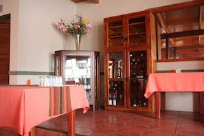Une pièce comprenant deux tables recouvertes de nappes rouges, un buffet en bois doté de portes en verre, et un vase rempli de fleurs posé sur une étagère.