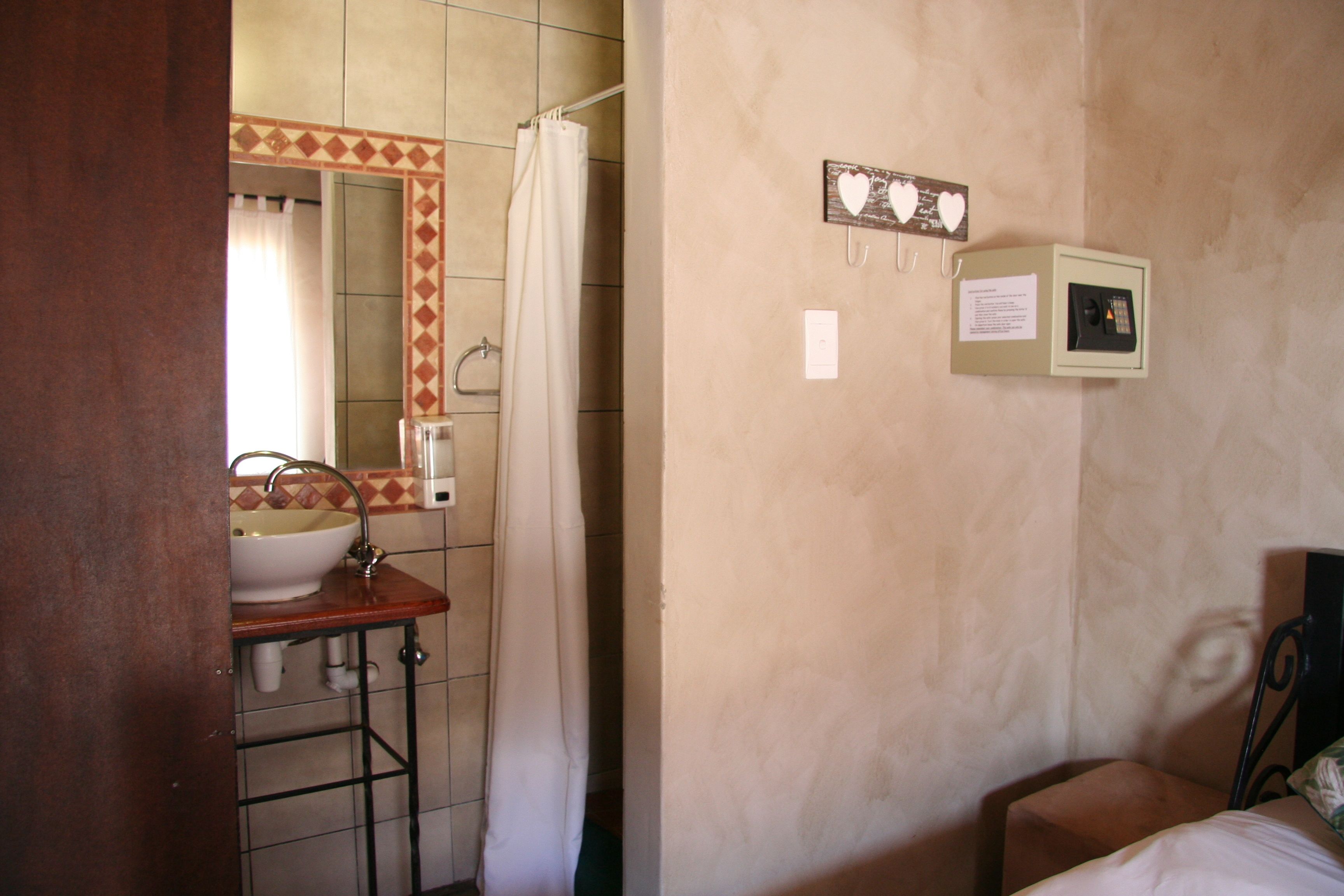 A bathroom with a sink, mirror, and shower curtain. There is a small cabinet with a paper note on the wall.