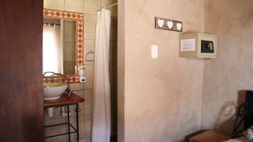 A bathroom with a sink, mirror, and shower curtain. There is a small cabinet with a paper note on the wall.
